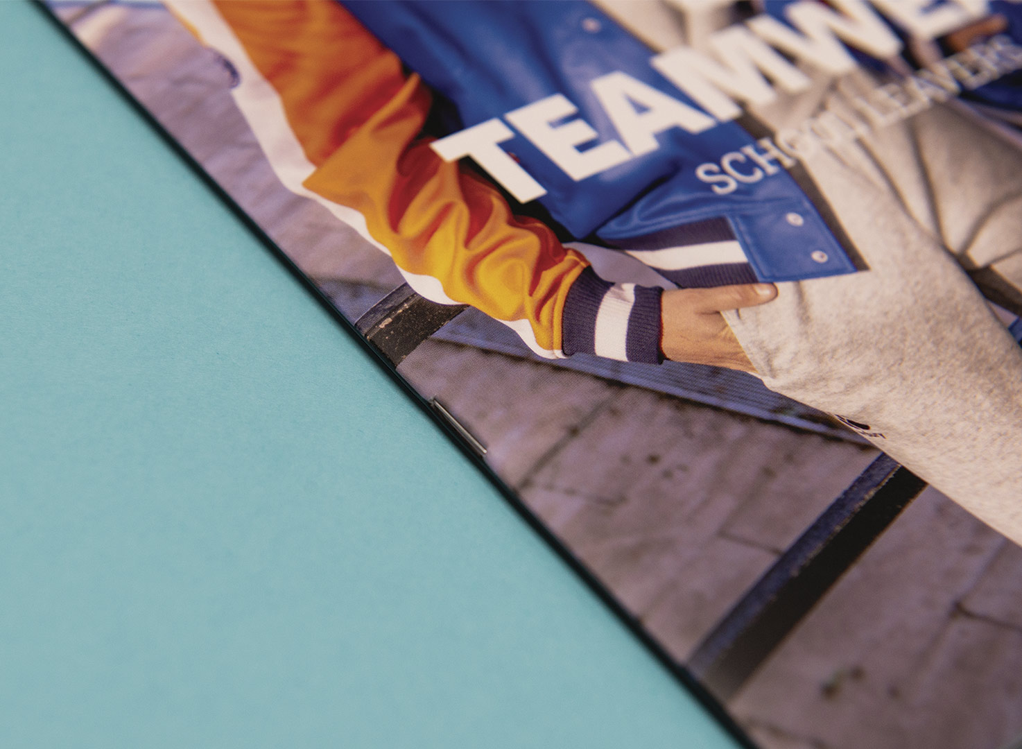 Close-up corner of a Canterbury Teamwear catalogue or magazine showing full-colour sports apparel photography on a teal backg